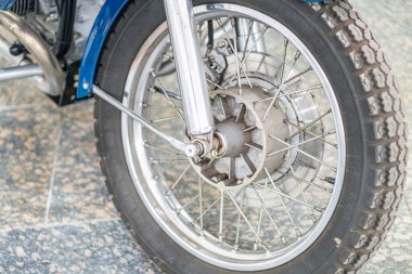 İyi bakımlı eski bir motorsiklet ön tekerleğinin yakın görüntüsü desenli lastik, parlak metal gövde, çevresel aydınlatma, açılı perspektif.