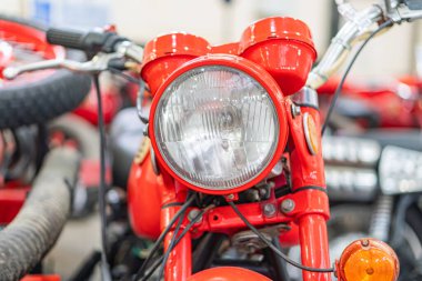 Kırmızı renkli bir motorsikletin kapalı bir ortamda, muhtemelen bir garaj ya da sergi salonunda yakın plan, far ve çerçeve, yumuşak gölgeli kırmızı renk düzeni, hatta aydınlatma bile, net bir görüntü oluşturur.