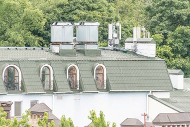 Üç katlı, kemerli pencereleri, fayanslı çatısı ve klima ve uydu antenleri gibi modern imkanları olan beyaz Avrupa binası, bulutlu bir günde yumuşak ışıklandırmayla çekiliyor.
