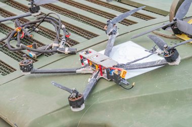 Küçük siyah beyaz kuadkopter drone, yıpranmış yeşil bir askeri kamyon yatak örtüsünün üzerinde duruyor.
