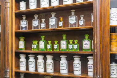 Bir eczane içinde antika bir dolap cam şişe koleksiyonu, çeşitli boyutlarda ve şekillerde etiketli kaplar, yeşil ve sarı tonlarda hatta yumuşak gölgeli aydınlatma bile organize kaos, ahşap p