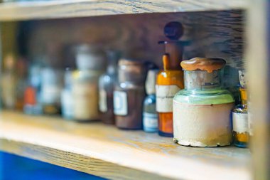 Bir eczanenin antika ahşap rafına yakın plan, çeşitli cam şişelerle dolu şişeler çeşitli şekil ve boyutlarda, kehribar rengine açık, kaplanmış veya mühürlenmiş farklı ışıklandırma