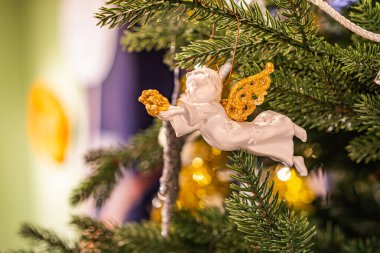 Porselen melek figürlü, altın boncuklu, çam yapraklı ve yumuşak gölgeli bir Noel ağacı dalının yakın görüntüsü.