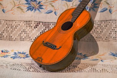 İyi kullanılmış ahşap bir gitar. Mavi çiçekli, beyaz bir altlık. Kapalı bir ortamda ayarlanmış.