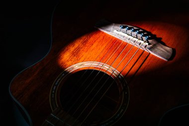 Akustik bir gitarın boynunun yakın plan görüntüsü, doğal ışık altında perdelere odaklanmış ahşap tonların ve metal perdelerin hakim olduğu ılık renk paleti fretboard ve bir kısmını içerir