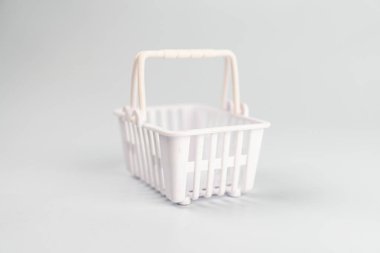 Mini kırmızı karikatür alışveriş arabası beyaz bir arka plana karşı, açık gri bir yüzey üzerinde duran tek bir hasır sepet