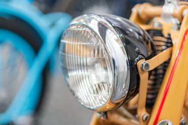 Kapalı bir ortamda, krom ve pirinç aksanlı, metalik kaplama, yumuşak ışıklandırma ve bulanık bir arka plan ile cam veya plastik far içeren klasik bir motosikletin yakın plan görüntüsü
