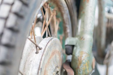 Eski bir motosiklet tekerleğinin yakın çekimi, açılı görüş, paslı jant kapağı, birden fazla tel, endüstriyel arka plan, monokrom renk şeması, gerçekçi tarz, doğal ışıklandırma, faydacı tasarım