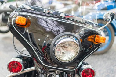 Siyah, klasik bir motosiklet yakın plan, belirgin farları, kehribar dönüş sinyalleri, ve olası krom ya da ayna kaplama bileşenleri kapalı alanda, yumuşak gölgeler başka bir aydınlatma önerir