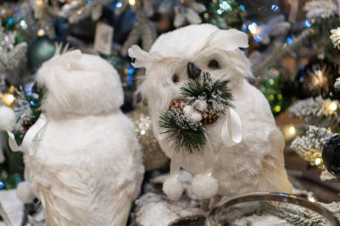 İki beyaz baykuş süslenmiş bir Noel ağacının dalında oturur, neşeli ışıklar ve çam kozalaklarıyla rahat bir tatil atmosferi, yumuşak gölgeler, sıcak renkler ve tuhaf bir tarzı vardır.