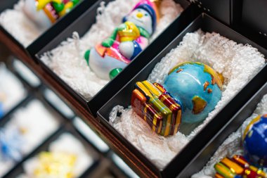 Siyah tribünlerdeki renkli, karmaşık detaylı cam Noel süsleri koleksiyonunun yakın çekimi, koyu bir arkaplan ile çelişiyor.