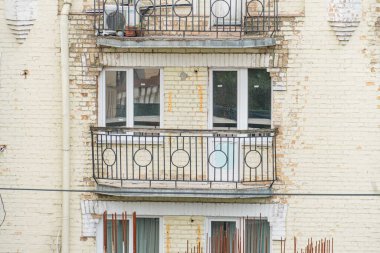 Metal parmaklıkları ve beyaz çerçeveli pencereleri olan çok katlı Avrupa binasının iki balkonu var. Bir balkonda bitki örtüsü var. Doğal ışık manzarayı aydınlatıyor.