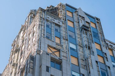 Açık çelik iskelet, cam ve beton paneller, uzun gölgeler ve dinamik bileşim ile karakterize edilmiş kentsel bir ortamda modern bina inşa ediliyor.