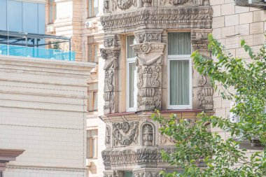 Eski bir Avrupa binasının ön cephesi, ağırlıklı olarak bej ve gri, karmaşık oymalar, dekoratif desenler, merkezi bir pencere ve muhtemel ek dekoratif elementler.