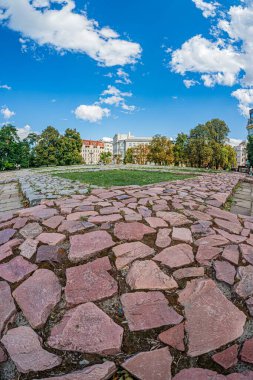 Eski bir Avrupa şehrinde sakin bir kaldırım taşı yolu. Birden fazla sütunu olan kırmızı çatılı bir binaya çıkıyor. Sahne sıcak ve toprak, dağınık ağaçlar ve bulutlar var.
