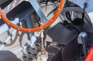 Retro Formula 1 yarış arabasının direksiyon simidinin yakın görüntüsü, ek kontrollerle bir merkeze monte edilmiş, karbon fiber iç kısımda birden fazla düğme ve çevirme ile detaylandırılmış gölgeli bir arka plan