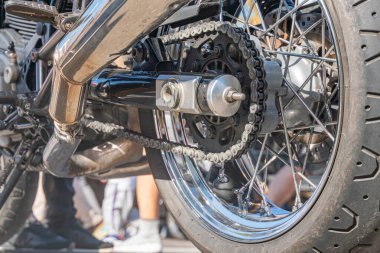 Siyah bir motosiklet lastiğinin yakın plan görüntüsü. Gümüş bir kenarda lastik izleri var. Zincir ve çıkıntıya bağlı.