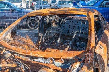 Çürüyen araçların ve nesnelerin arasında terkedilmiş, yanmış bir araba.