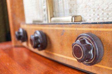 Pirinç aksanlı eski bir ahşap boru radyo, sıcak ışık altında bulanık bir iç yüzey üzerine yerleştirilmiş dikdörtgen radyo ayarlama ve ses kontrolü için dört düğmesi vardır.