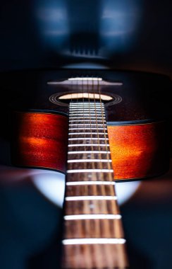 Spot ışıkları altında iyi korunan akustik gitarın yakın plan çekimi ayrıntılı fretboard ve telleri gösterir. Karanlık vücut, daha hafif boyun kontrastı kontrastı, potansiyel olarak müzik reklamları için.