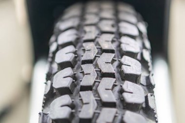 Bulanık asfalta karşı gri-siyah, parlak bir off-road tekerleğinin yakın plan görüntüsü.