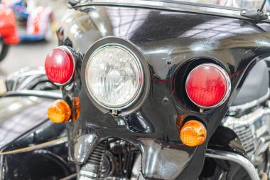 Yuvarlak farlı, krom ızgaralı, suni ışığın altında park edilmiş siyah klasik motosiklet müze sergisi veya galerisinde diğer klasik motosikletlerle çevrili.