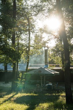 Kyiv, Ukrayna 06-26-2025 'teki açık hava mobilyaları, odun yığınları ve güneşli desenler, uzun ağaçlarla çevrili ve çitlerle çevrili bir açık hava manzarası.