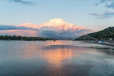 Köprüsü olan bir göl manzarası, pinkorange gökyüzü, altın saat aydınlatma, su üzerindeki tekne, canlı renkler, sakin manzara, açık gökyüzü yansıması, metin yok Kyiv, Ukrayna 06-29-2025