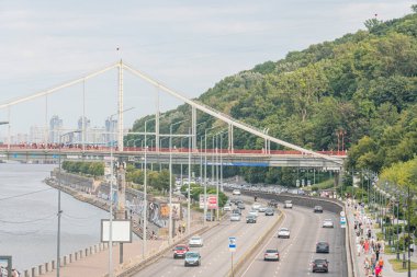 Ukrayna 'nın başkenti Kyiv, Ukrayna' da güneş doğarken veya batarken bir asma köprüye ev sahipliği yapan köprü, Ukrayna 07-06-2025 no 'lu yol üzerindeki destek, kablolar ve güverte görünür araçları yerleştirdi.