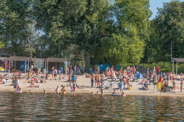 İki perspektiften Kyiv plaj sahnesi yoğun bir kumlu plajı gösteriyor, insanlar havluların üzerinde oturuyor, cankurtaran kulesi, bulutlu gökyüzü, Kyiv, Ukrayna 07-12-2025
