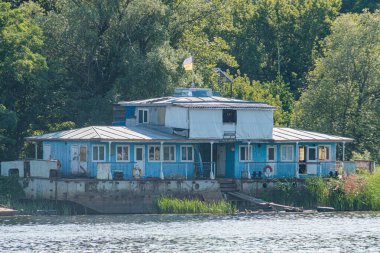 Rustik, Ukrayna 'nın başkenti Kyiv' de yemyeşil ve bulutlu bir nehir kıyısındaki terk edilmiş iki katlı binada geleneksel ahşap yapının deca Kyiv, Ukrayna 07-12-2025 işaretleriyle aydınlatılması planlanıyor.