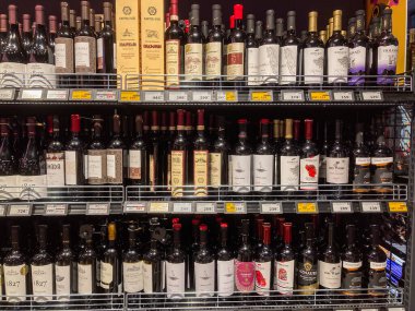 İyi stoklanmış bir şarap deposu, çeşitli şekil ve renklerde çeşitli şarap şişeleriyle dolu, marka isimleri ve yıllarla etiketlenmiş, Kyiv, Ukrayna 07-02-2025