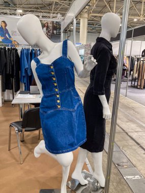 Parlak bir mekanda iki ana mankenin yer aldığı moda sergisi. Bir manken dikey sarı çizgili açık mavi bir kot elbise giyerken, diğeri Kyiv, Ukrayna 07-31-2025