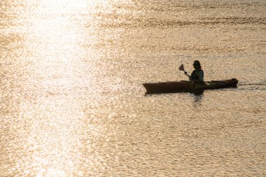 Sakin suda kano benzeri bir teknede tek bir kürekçi, sıcak tonlarda sessiz renk paleti, hafif dağınık ışık Kyiv, Ukrayna 06-05-2025