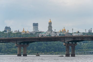 Dinyeper Nehri 'nin karşısındaki Kyiv şehrinin manzarasında, altın kuleye sahip modern cam gökdelenler ve uzun süspansiyon köprüsü Kyiv, Ukrayna 06-14-2025