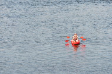 Kırmızı kanoyla tek başına, sakin mavi-yeşil suda, uzağa bakan, küreği tutan, beyaz gömlek, güneşli gün, yumuşak gölgeler Kyiv, Ukrayna 07-04-2025