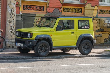 Gri bir yola park edilmiş sarı renkli arazi aracı. Arkaplanı grafiti, bulutlu gökyüzü Kyiv, Ukrayna 07-05-2025