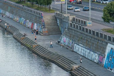 Kyiv 'deki şehir manzarası, Ukrayna Grafiti ile süslenmiş nehir kenarındaki taş duvar, nehir kenarındaki insanlar, uzak bir yoldaki arabalar, sabahın erken saatlerinde ya da öğleden sonra Kyiv, Ukrayna, 07-05-2025