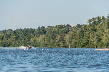 Güneşli bir günde Ukrayna 'nın başkenti Kyiv' de sakin göl manzaraları arasında jet ski, parasailing ve yüzme ağaçlarının yoğun sınırı Vibrant yeşillikleri Kyiv, Ukrayna 07-12-2025 kontrastı