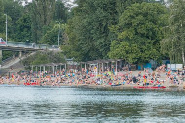 Ukrayna 'nın başkenti Kyiv' de canlı bir sahil manzarası. Parlak güneş ışığı altında göktaşı suları altında dağınık teknelerle kumsalda dinlenen insanlar ve Ukrayna 'nın Kyiv kentinde yemyeşil bir orman.