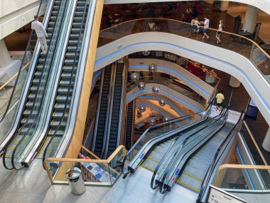 Eğri yürüyen merdivenleri, merkezi dairesel yapısı, gri ve kahverengi renk paleti, çoklu seviyeler, eşit dağılmış aydınlatma, banklar, Kyiv, Ukrayna 08-03-2025