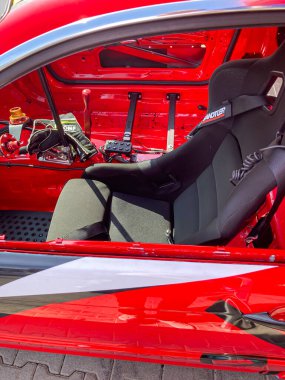 Kokpitte soyulmuş kırmızı drift araba, açık şasi ve motor, yeni ve yıpranmış parçaların karışımı, siyah kova koltuk, emniyet kemeri, gri beton arka plan, gün ışığı Kyiv, Ukrayna 06-15-2025