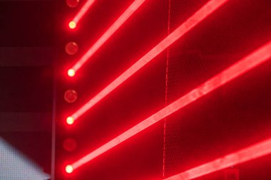 Lazer şovu sahne sahnesi, canlı kırmızı ve beyaz ışıklandırma, geniş renkli ekran gösterim daireleri, ekip elemanlarının araç gereçleri, yukarı bakış açısı, samimi tarz, canlı müzik performansı.