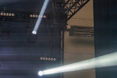 Sahne ışıkları tarafından aydınlatılan konser sahnesi, sahnenin etrafına dağılmış dinamik ve dramatik bir atmosfer yaratıyor. Arka plan bulanıklaşması sahne dışı aktiviteye işaret ediyor.