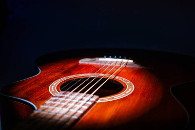 Yaş, koyu kahverengi akustik gitarın yakın çekimi dairesel ses deliği desenli yumuşak ışıklandırma ve sığ alan derinliği enstrümanı kapalı bir ortamda izole eder.