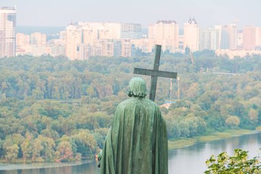 Kyivs Cross on the Water 'da sakin bir manzara, kentsel bir siluete karşı haç tutan yeşilimsi metal bir heykelin heykeli The composit Kyiv, Ukrayna 07-08-2025