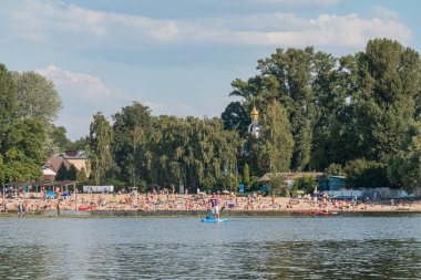Ukrayna 'nın başkenti Kyiv' deki güneşli sahil manzarası kişisel eşyalar ve küçük teknelerle deniz kenarındaki kuma saçılmış durumda. Ağaçlar doğal bir sınır olan Kyiv, Ukrayna 07-12-2025