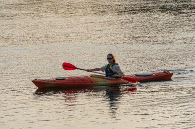 Gün batımında dalgalı suda kürek çeken bir adam, günbatımında açık havada kano ve kürekleri kullanılıyor, altın ışıklı banyo sahnesi, sakin atmosfer Kyiv, Ukrayna 06-05-2025