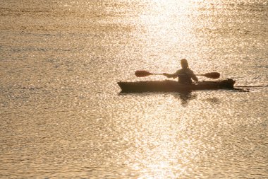 Gün batımında suyun sakin gövdesinde bir kişi, sağa doğru hareket ediyor, sıcak ve serin renk tonları, dalgalı doku, kürek, hafif oyun, yalnızlık, doğal Aziz Kyiv, Ukrayna 06-05-2025