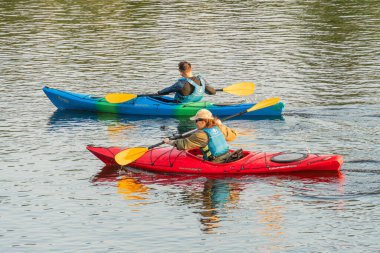 Can yelekli iki kişi kırmızı, mavi kürek çeken ayrı bir su aracı kanosu - kırmızı, yeşil kano - sakin su bulutlu gün veya sabahın erken saatlerinde aydınlatma Kyiv, Ukrayna 06-05-2025